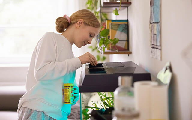 A young woman drops pellets of fish food into her home's aquarium situated in the home's living room
