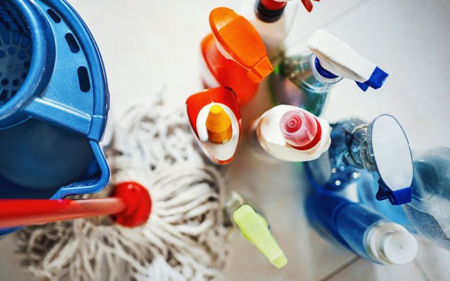 Overhead view of a number of bottles containing cleaning solutions with a mop standing next to them on the floor of a house
