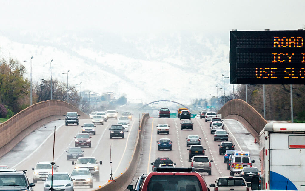 A view of an interstate highway filled with vehicles traveling in both directions, as a DOT sign warns of winter weather road conditions