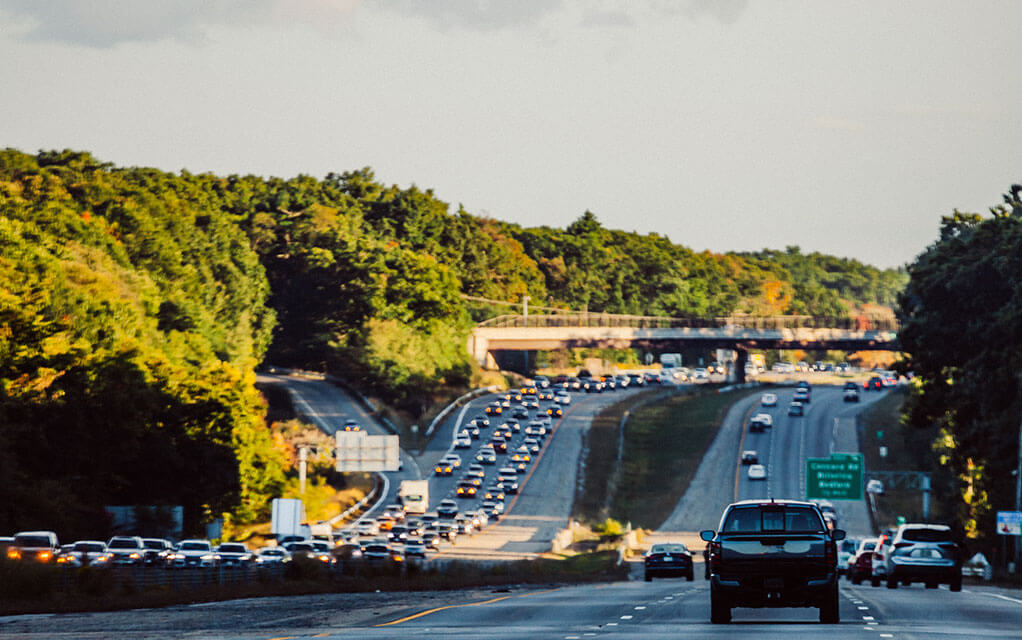 Heavy traffic lines one side of a busy highway as vehicles travel in both directions on a sunny late afternoon day