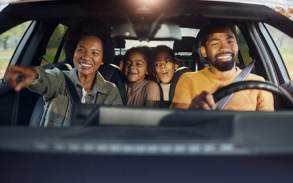 A happy family is in their car on a trip as the mother points to a roadside destination that is out of view