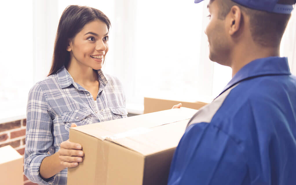 A woman hands off a box to a professional mover in her home