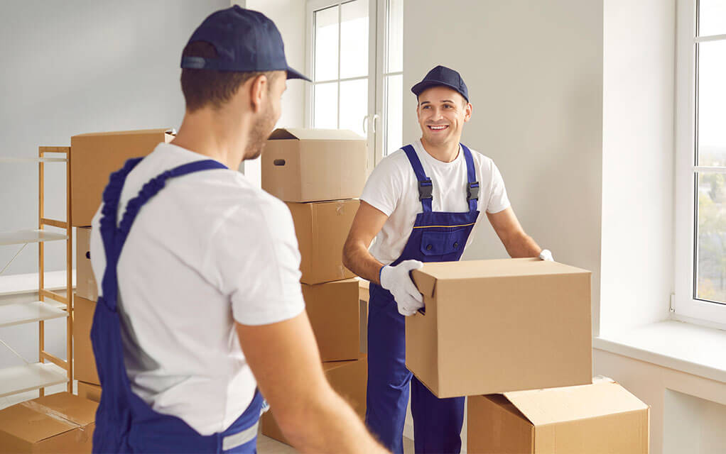 Two professional laborers seem to joke with each other, as the one in the background grabs hold of a box, ready to take it out of the home