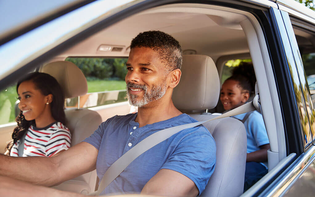 A middle-aged man and woman with their young daughter in the back seat set off for a drive in their vehicle on a sunny day