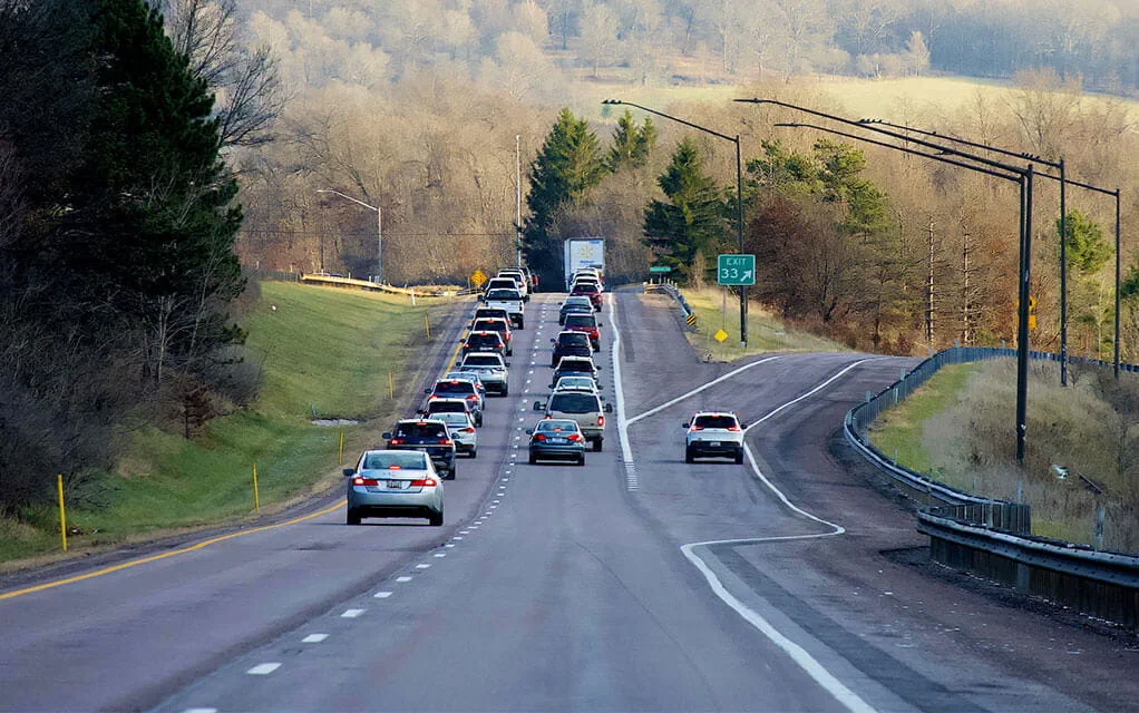 View of a pack of cars and traffic passing a highway exit in the late afternoon of a fall season day as the light begins to fade