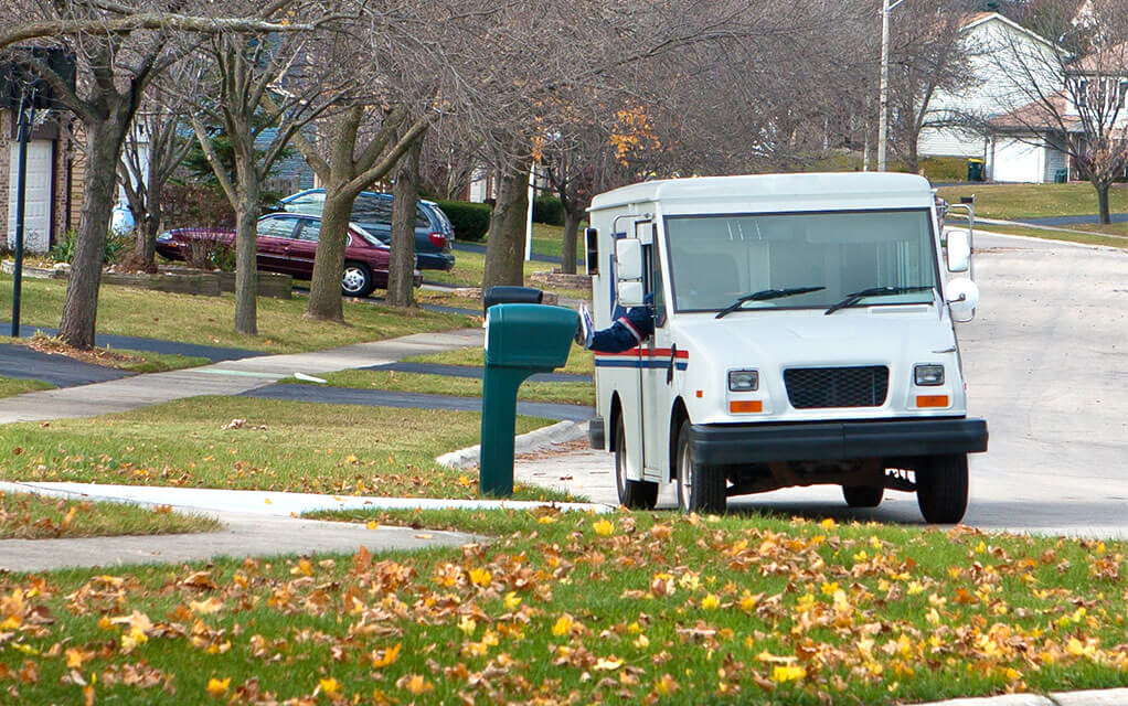 A USPS mail carrier in their truck is delivering mail in a suburban neighborhood on a cloudy Fall afternoon
