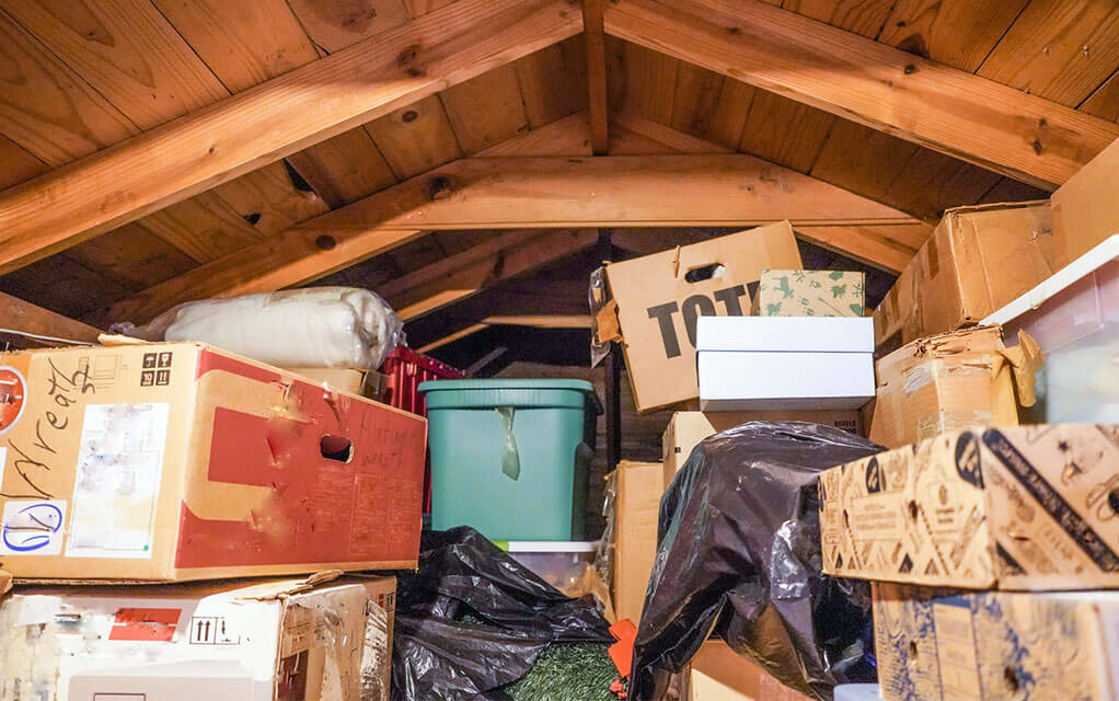 A pile of boxes, bins, and other stored items are haphazardly stacked on top of each other in the attic of a home