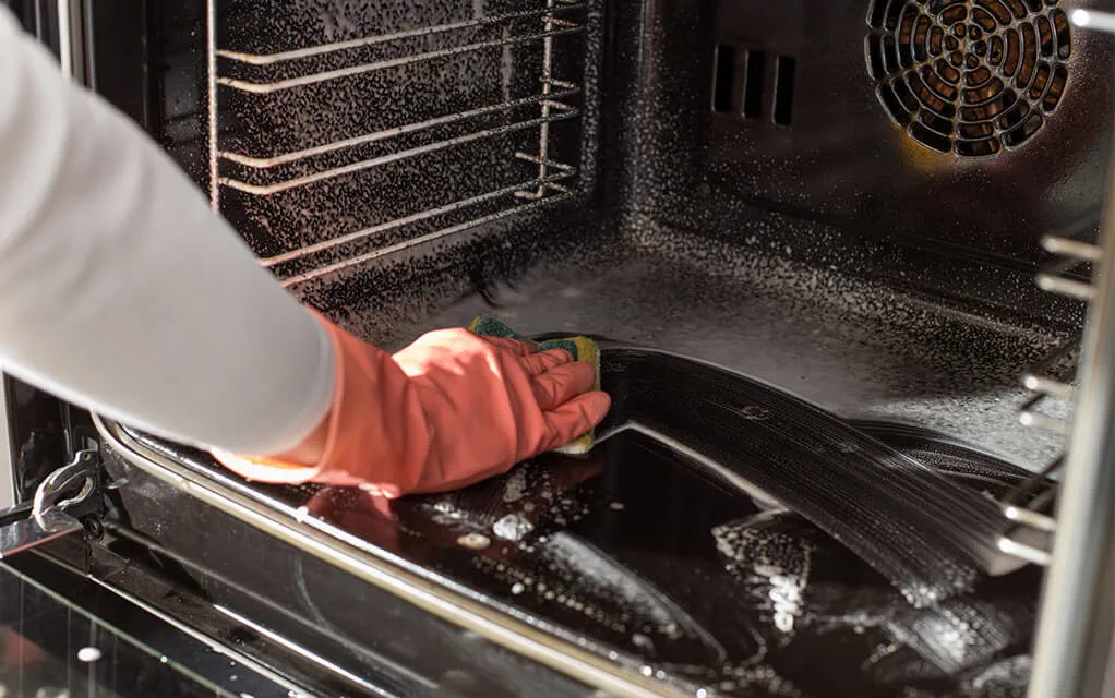 A person wearing protective gloves cleans the inside of their oven 