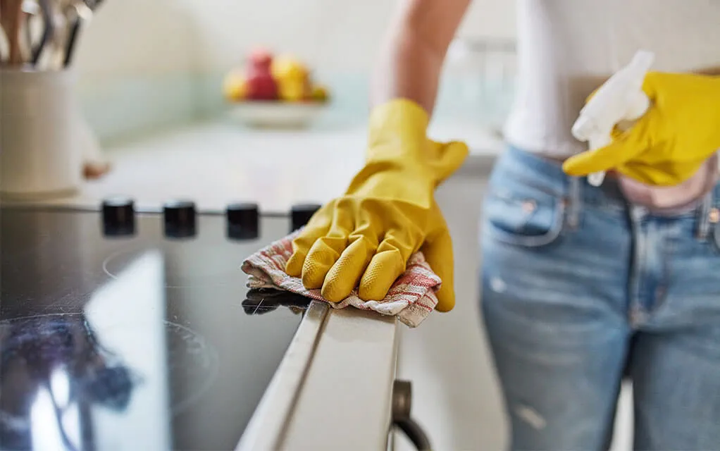 A person cleans their kitchen stovetop while wearing yellow gloves