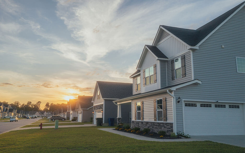 View down a quiet suburban street lined with nice looking homes as the sun rises in the background on a clear morning
