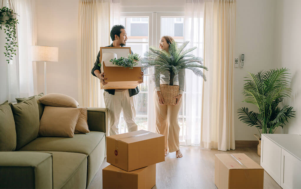 A happy couple brings plants and boxes into their new home on a sunny day