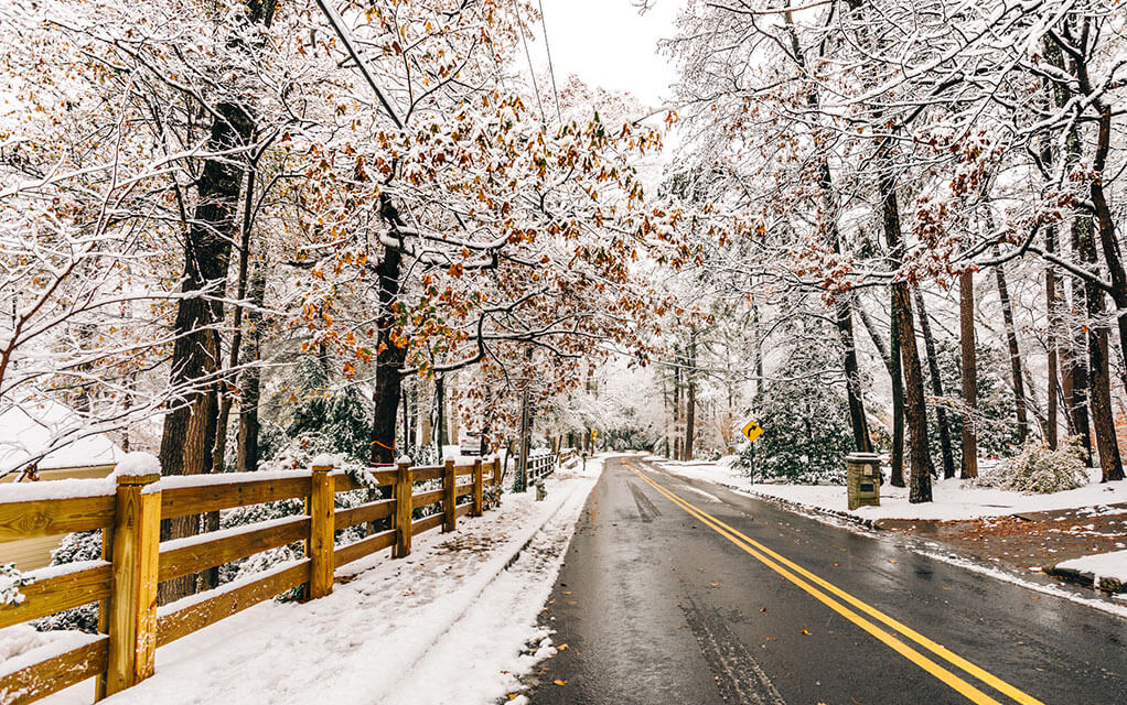 View down a back country road that looks a little icy as snow and ice cover the ground and trees
