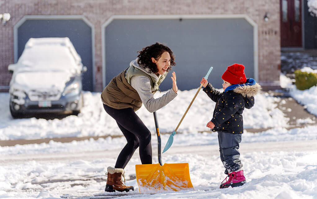 A mother and her young daughter high five each other as they help clean snow and ice off their home's driveway