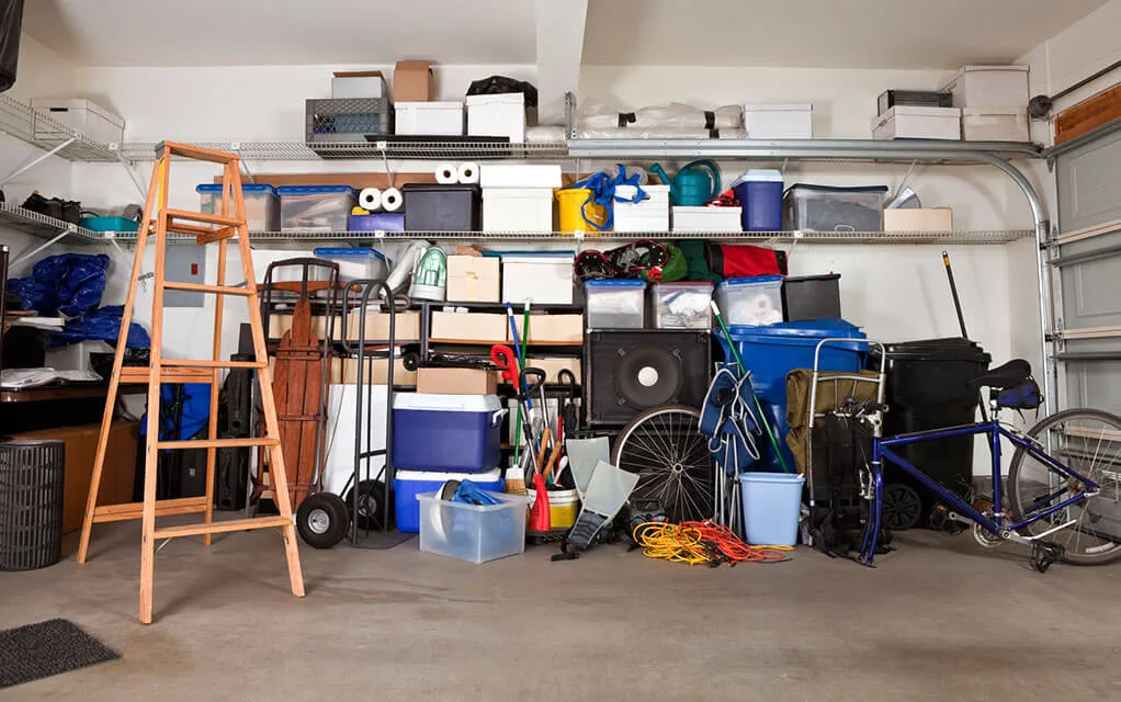 A bunch of boxes and other items are piled against the wall inside of a home's garage