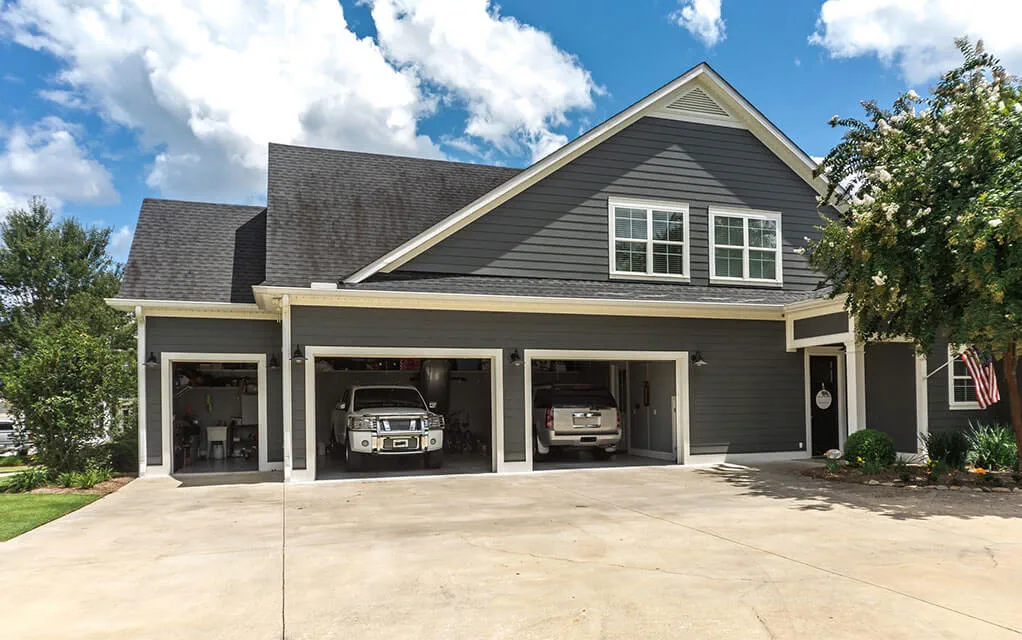 View of a gray colored upscale home with it's three garage doors open with vehicles sitting inside