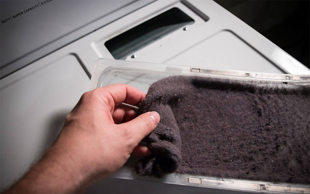 A person is removing a large amount of collected lint off of a dryer's lint filter