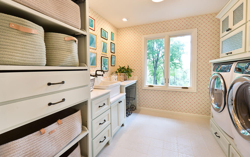 A view of an upscale home's laundry room, complete with shelving, storage, a sink, windows overlooking the home's yard, and a washing machine and dryer matching pair.