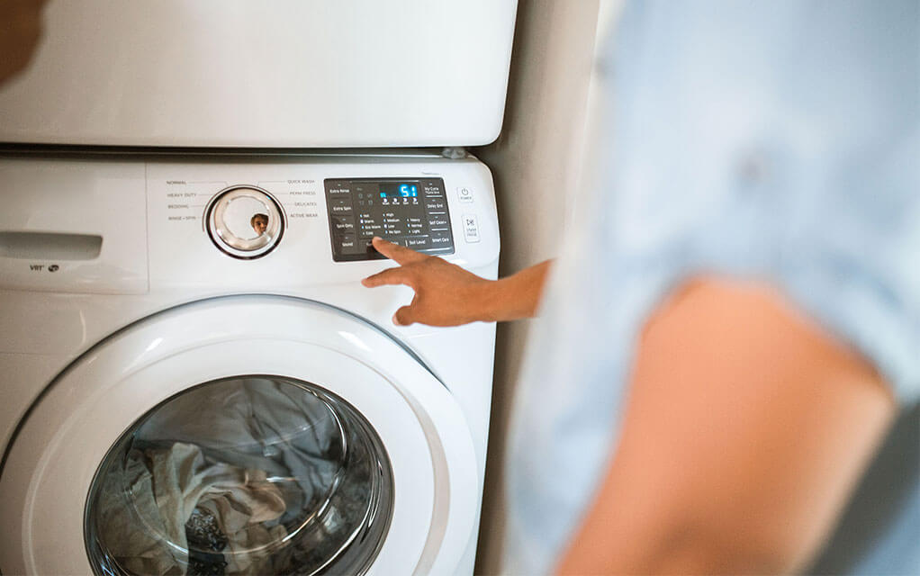 A person inputs commands into the interface of a washing machine to begin a cleaning cycle of their clothing