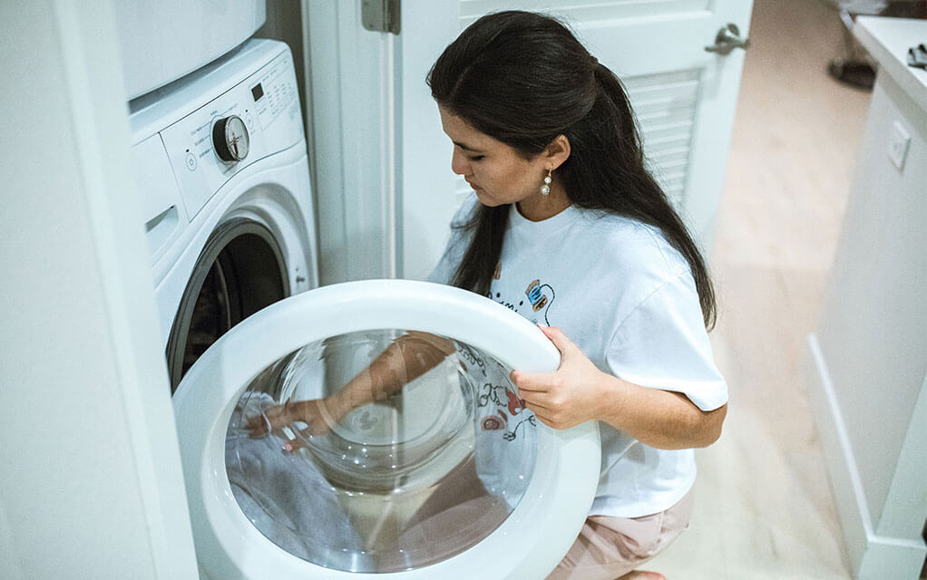 A woman kneeling on the floor places clothes into her home's washing machine