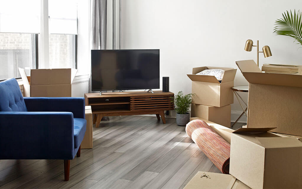 A turned off TV sits on an entertainment center waiting to be packed away as unpacked boxes lay around it with other items waiting to be moved