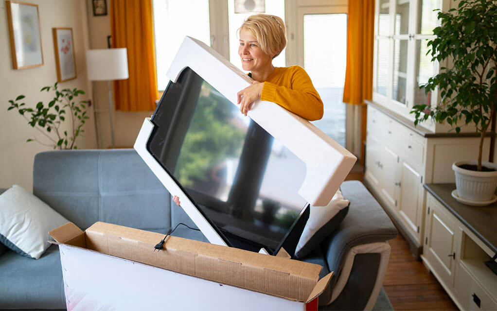 A middle-aged woman is packing her TV away into a tailor made TV moving box on a sunny day