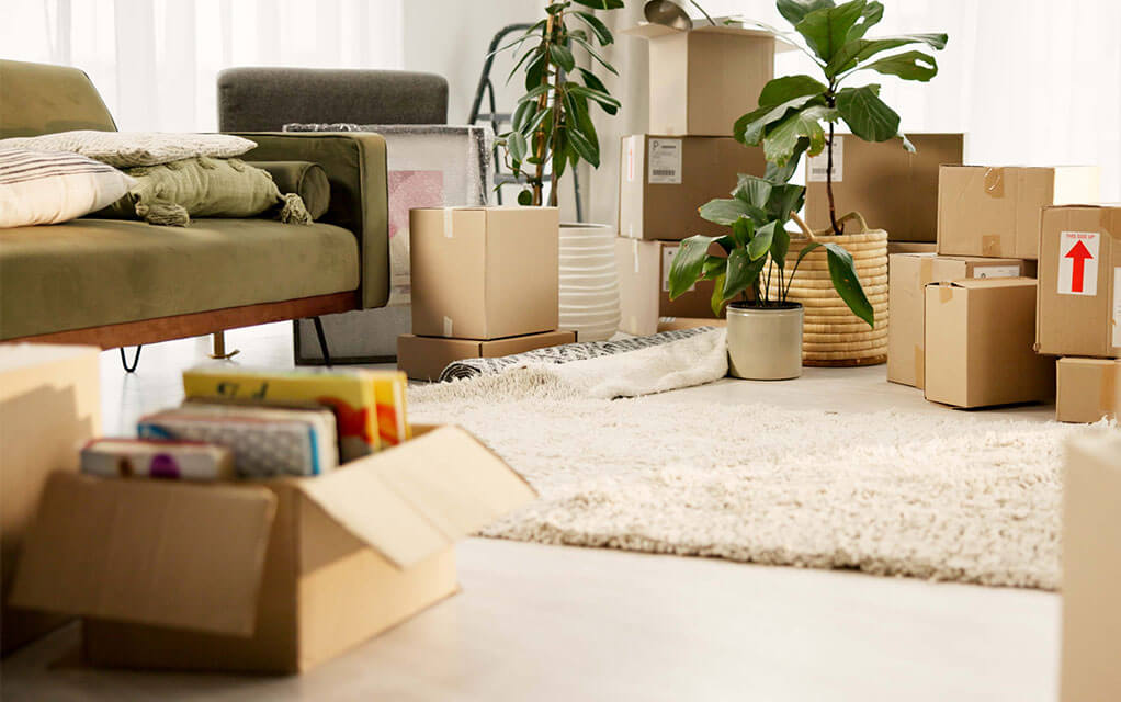 A pile of moving boxes, both closed and open sit on the floor of a home ready to be packed away with other belongings and furniture