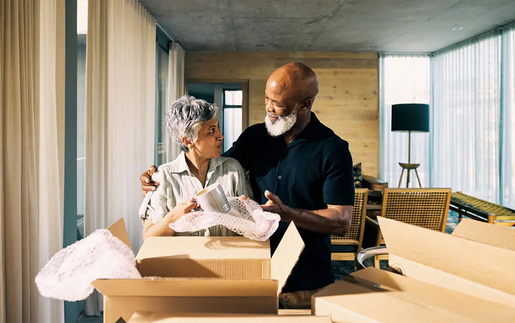 An older couple begin to unpack moving boxes in their new home on a bright day