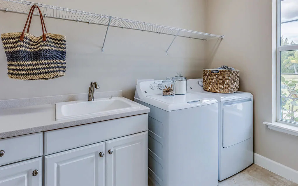 A washer and dryer set sits in a home laundry room with a sink in it as sun comes through the window