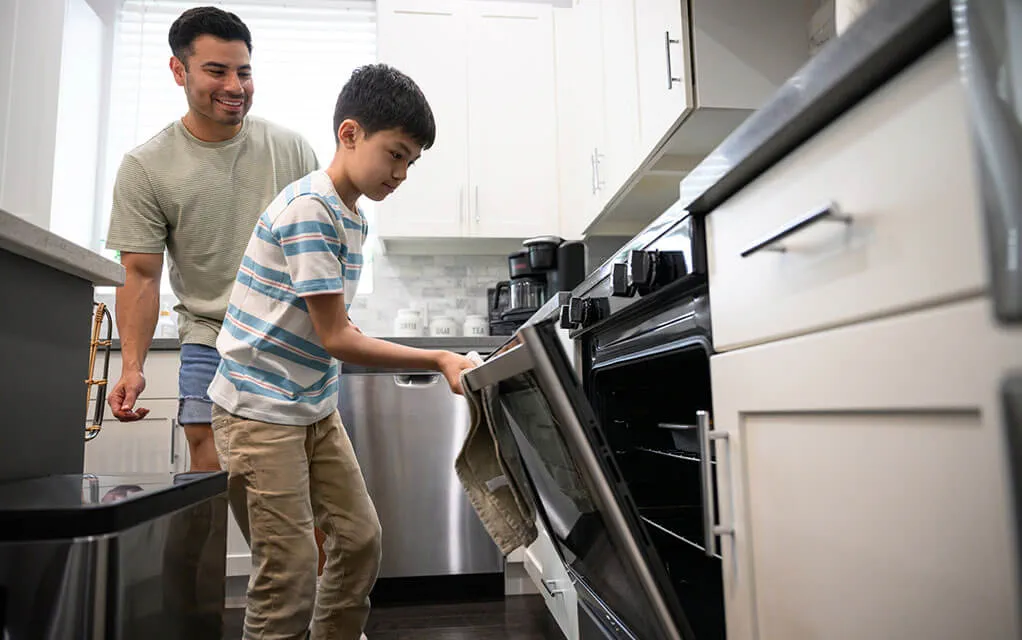 A father and son prepare some food as the son opens the kitchen oven