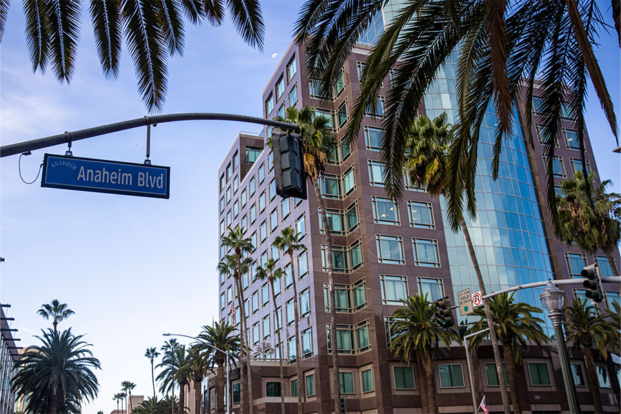 A view of downtown Anaheim, CA, with the Anaheim Blvd street sign in view in front of a large building on a bright, sunny day